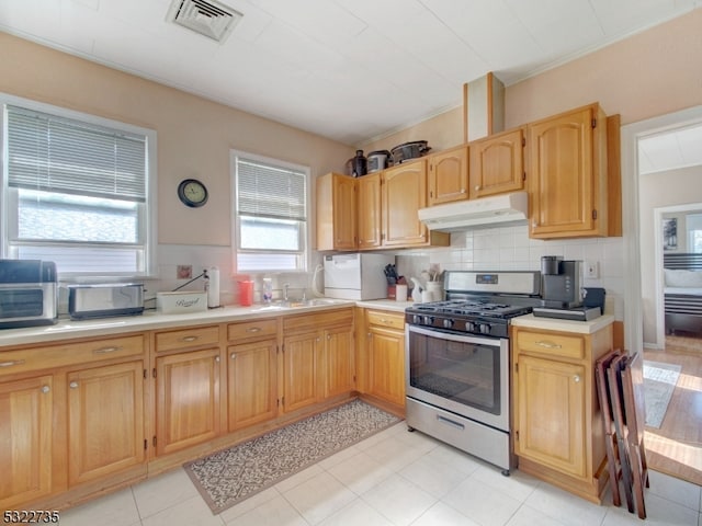 kitchen featuring tasteful backsplash, light tile patterned floors, light brown cabinets, sink, and stainless steel range with gas stovetop