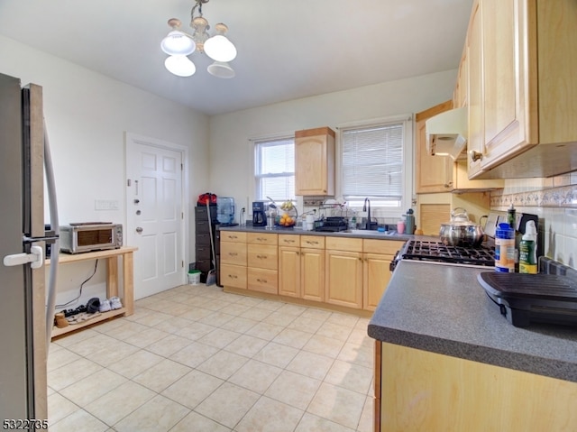 kitchen with stainless steel appliances, exhaust hood, light brown cabinetry, and an inviting chandelier