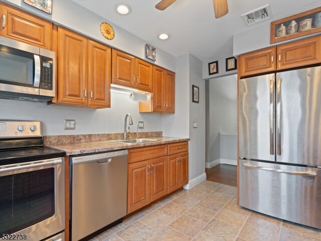 kitchen with stainless steel appliances, sink, ceiling fan, and light stone countertops