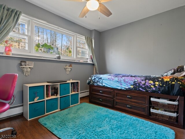 bedroom with baseboard heating, dark wood-type flooring, multiple windows, and ceiling fan