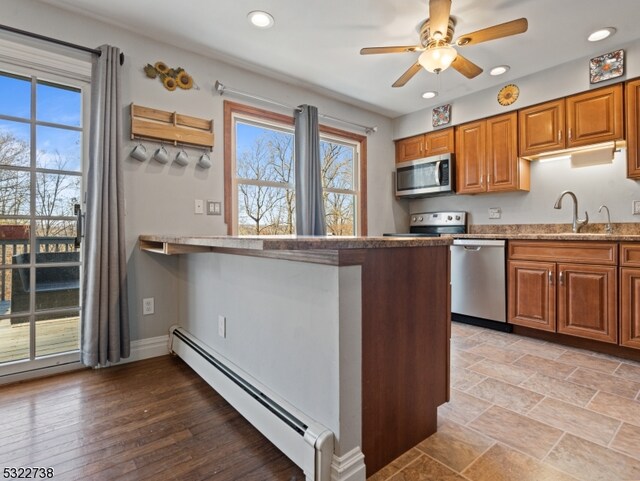 kitchen featuring stainless steel appliances, sink, baseboard heating, ceiling fan, and light wood-type flooring