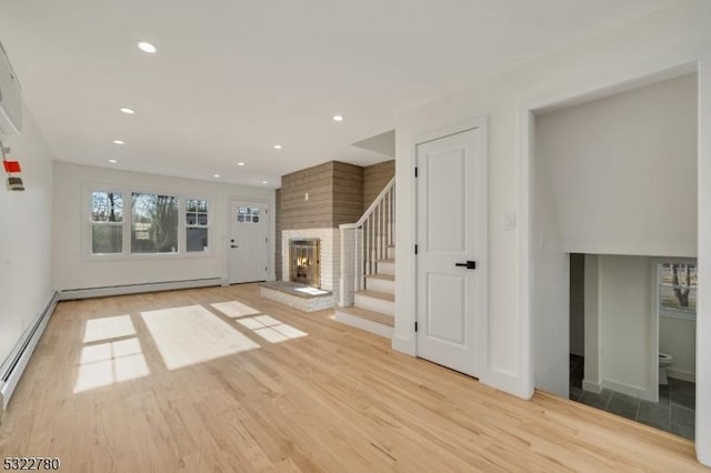 unfurnished living room with a large fireplace, light hardwood / wood-style floors, and baseboard heating