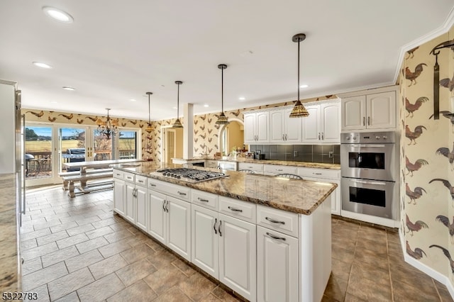 kitchen with stainless steel appliances, a kitchen island with sink, white cabinetry, and decorative light fixtures