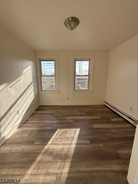 empty room featuring dark wood-type flooring, plenty of natural light, and a baseboard heating unit