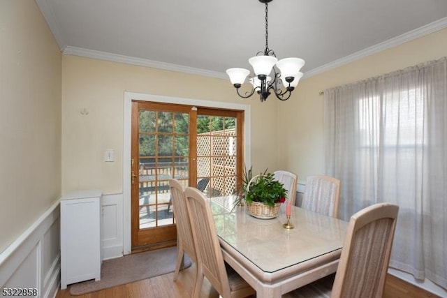 dining space featuring light wood-style floors, a wainscoted wall, crown molding, and an inviting chandelier