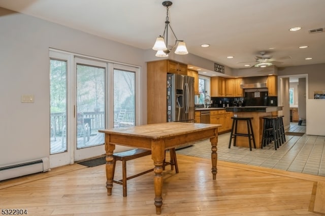 dining room featuring baseboard heating, light hardwood / wood-style floors, and ceiling fan with notable chandelier