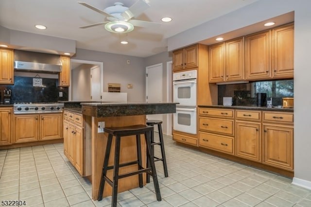 kitchen featuring a kitchen bar, a center island, stainless steel gas cooktop, double oven, and backsplash