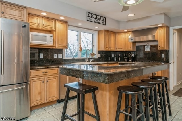 kitchen with a kitchen bar, wall chimney exhaust hood, light tile patterned flooring, backsplash, and stainless steel refrigerator