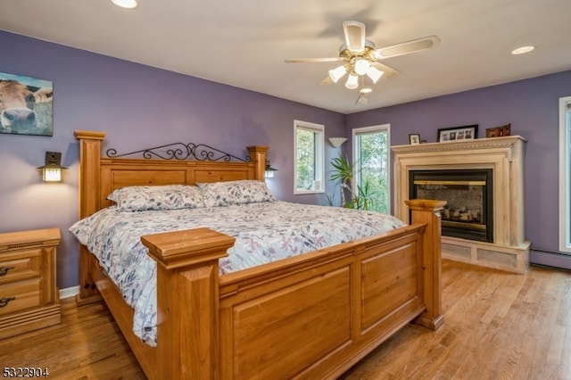 bedroom with ceiling fan, light hardwood / wood-style flooring, and a baseboard heating unit