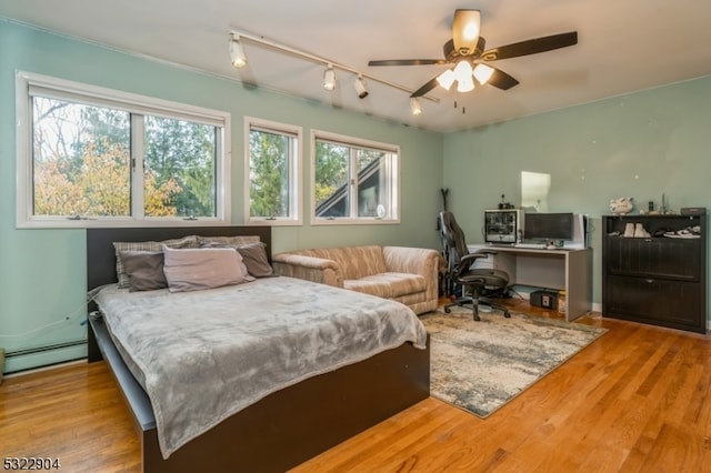 bedroom featuring a baseboard heating unit, light wood-type flooring, multiple windows, and ceiling fan