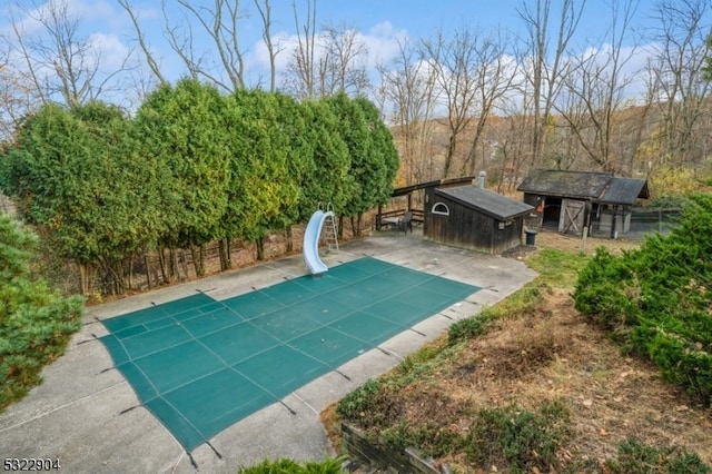 view of swimming pool featuring a water slide, an outdoor structure, and a patio