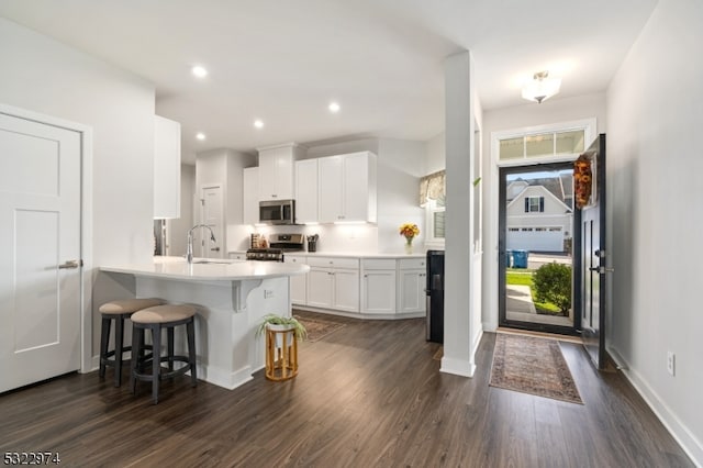 kitchen with stainless steel appliances, white cabinetry, dark hardwood / wood-style floors, a kitchen breakfast bar, and kitchen peninsula