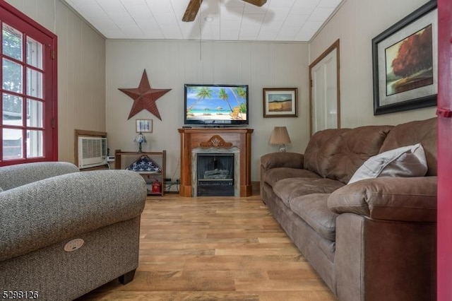 living area with a wall unit AC, ceiling fan, a fireplace, and light wood finished floors