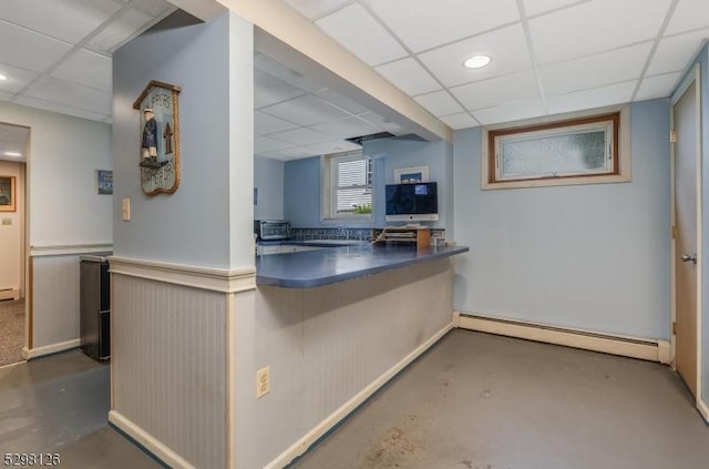 kitchen featuring a toaster, baseboard heating, finished concrete flooring, and a drop ceiling