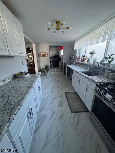 kitchen featuring a notable chandelier, sink, stainless steel range with gas cooktop, light stone countertops, and white cabinetry