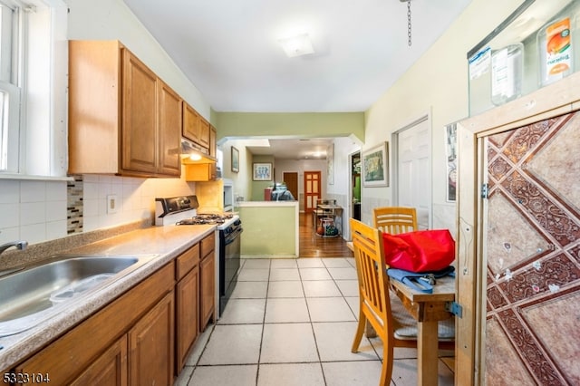 kitchen featuring backsplash, light tile patterned floors, white range with gas cooktop, and sink