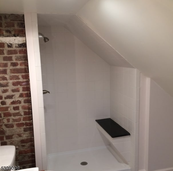 bathroom featuring tiled shower and brick wall