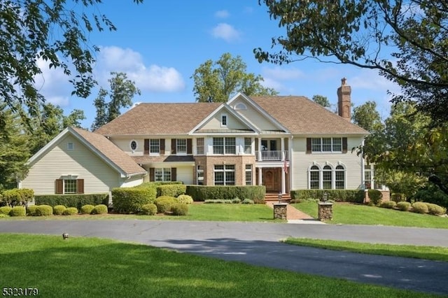 view of front facade featuring a balcony, a chimney, and a front lawn