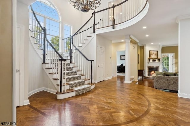 foyer with a large fireplace, baseboards, a towering ceiling, and ornate columns