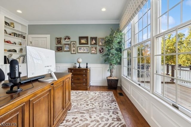 office with a wainscoted wall, dark wood-type flooring, visible vents, and crown molding