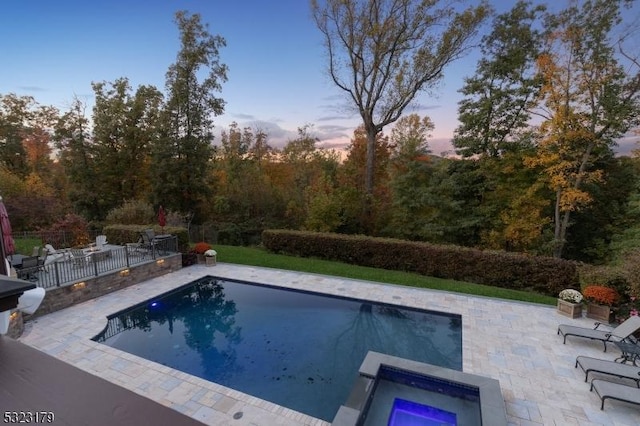 pool at dusk featuring fence, an outdoor pool, and a patio