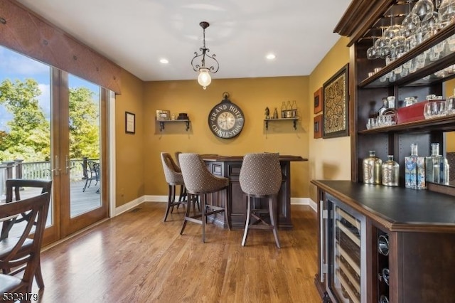 bar featuring beverage cooler, wood finished floors, baseboards, a bar, and decorative light fixtures