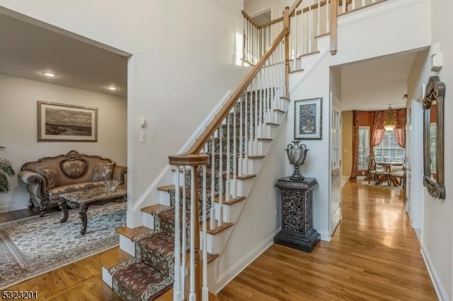 staircase with wood-type flooring and a towering ceiling