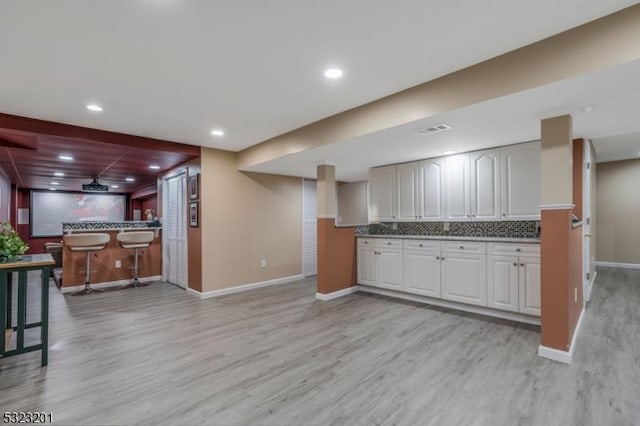 kitchen with backsplash, white cabinetry, a breakfast bar area, and light wood-type flooring