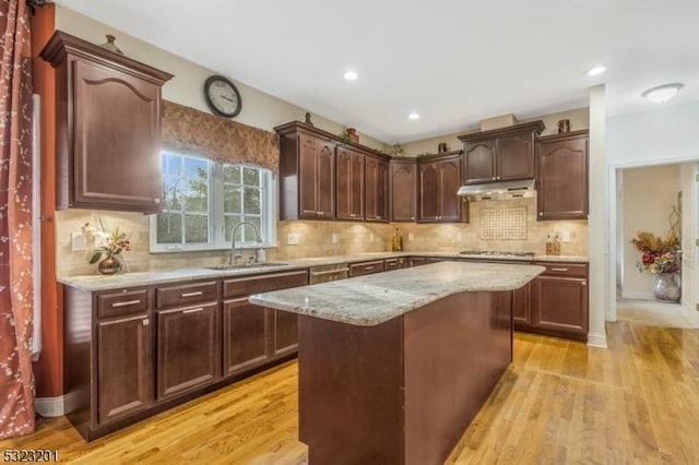 kitchen featuring stainless steel gas cooktop, sink, light wood-type flooring, a kitchen island, and light stone countertops