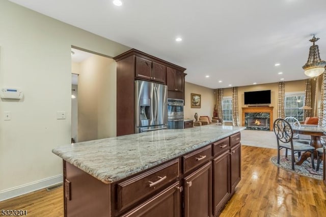 kitchen with dark brown cabinetry, stainless steel fridge, a kitchen island, pendant lighting, and light hardwood / wood-style floors