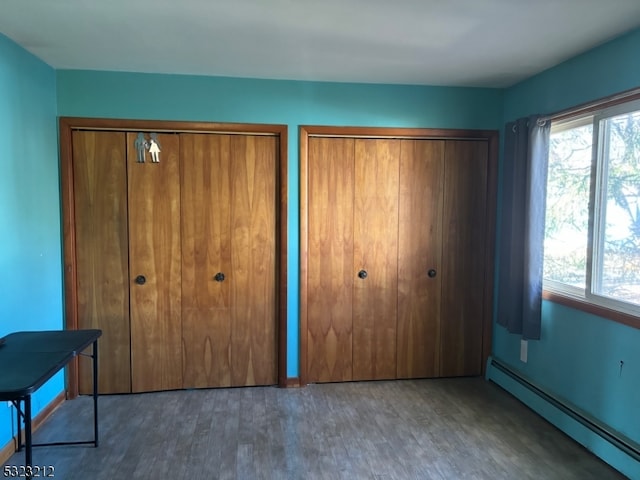 unfurnished bedroom featuring baseboard heating, multiple closets, and dark wood-type flooring