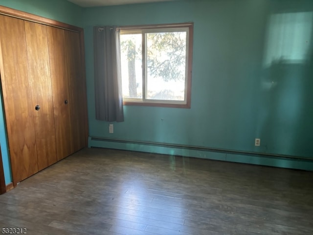 unfurnished bedroom with a closet, a baseboard heating unit, and dark hardwood / wood-style flooring