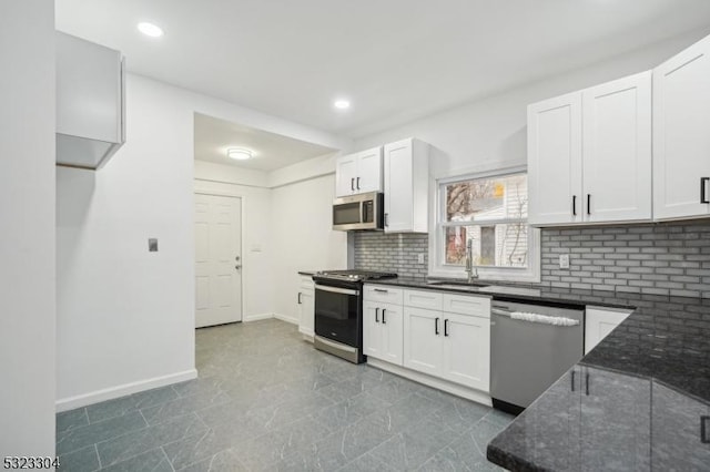 kitchen featuring stainless steel appliances, a sink, white cabinetry, dark stone counters, and tasteful backsplash