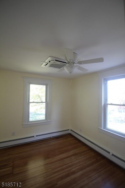 empty room with dark hardwood / wood-style flooring, a wealth of natural light, ceiling fan, and a baseboard heating unit