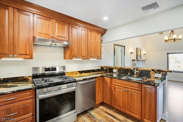 kitchen with light hardwood / wood-style floors, sink, kitchen peninsula, appliances with stainless steel finishes, and dark stone counters