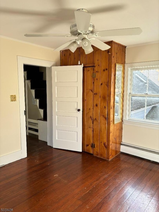 spare room with baseboard heating, crown molding, ceiling fan, and dark wood-type flooring