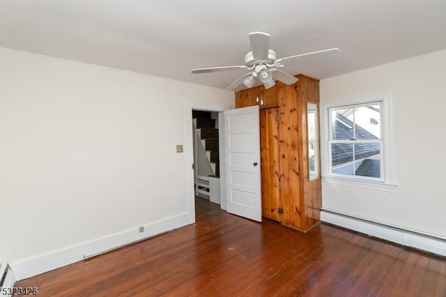 interior space featuring wooden walls, a baseboard radiator, ceiling fan, and dark wood-type flooring