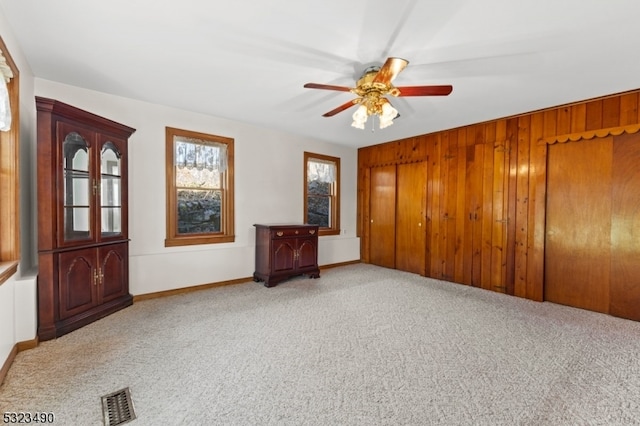 empty room with wood walls, ceiling fan, and carpet floors