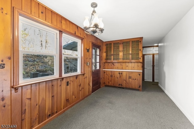 carpeted spare room featuring a chandelier and wooden walls