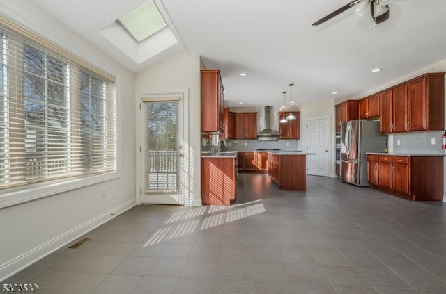 kitchen featuring a center island, stainless steel refrigerator with ice dispenser, hanging light fixtures, vaulted ceiling with skylight, and wall chimney exhaust hood