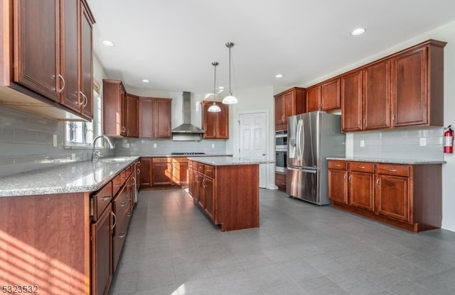 kitchen with sink, a center island, wall chimney range hood, decorative light fixtures, and appliances with stainless steel finishes