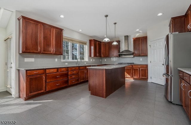 kitchen featuring a center island, backsplash, wall chimney exhaust hood, decorative light fixtures, and stainless steel refrigerator