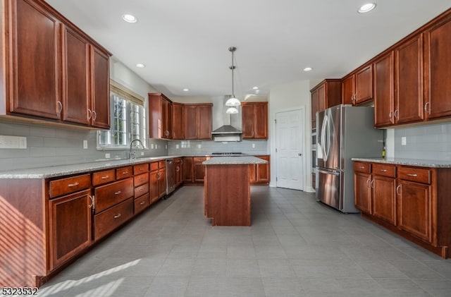 kitchen featuring a center island, wall chimney range hood, hanging light fixtures, light stone countertops, and appliances with stainless steel finishes