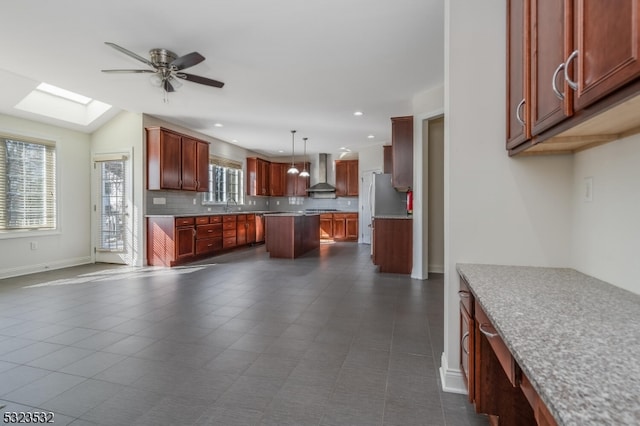 kitchen featuring backsplash, ceiling fan, sink, wall chimney range hood, and pendant lighting