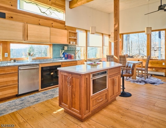 kitchen featuring appliances with stainless steel finishes, light wood-type flooring, decorative light fixtures, beamed ceiling, and a kitchen island