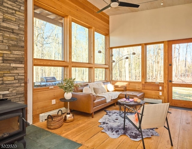 sunroom / solarium with a wood stove, ceiling fan, and a baseboard heating unit