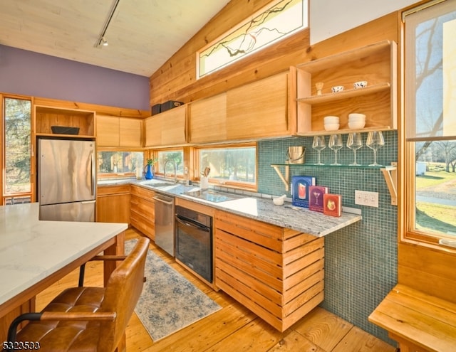 kitchen featuring light wood-type flooring, stainless steel appliances, vaulted ceiling, sink, and wood walls