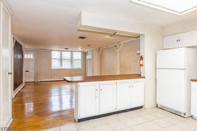 kitchen with white cabinets, light wood-type flooring, baseboard heating, white fridge, and kitchen peninsula