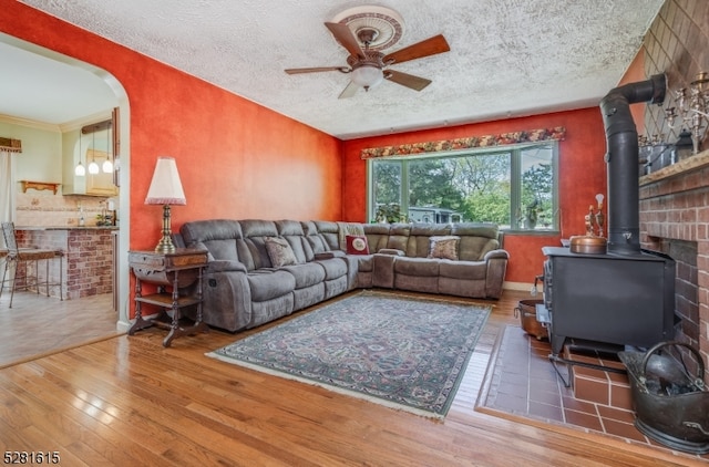 living room with ornamental molding, a textured ceiling, a wood stove, hardwood / wood-style flooring, and ceiling fan