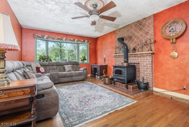 living room with hardwood / wood-style flooring, ceiling fan, a textured ceiling, and a wood stove